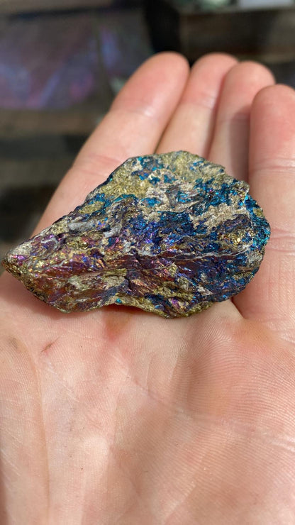 Morceau brut de chalcopyrite aux reflets dorés, bleus et violets présenté dans une main