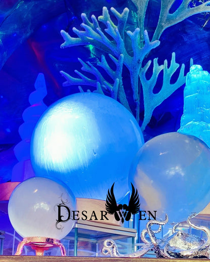 Grande sphère de sélénite éclairée en bleu parmi d’autres sphères et un décor marin