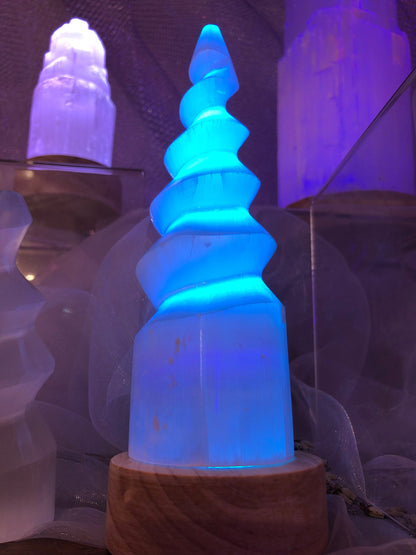 Lampe en spirale de sélénite éclairée en bleu turquoise sur son socle en bois