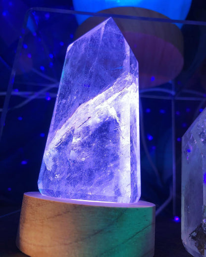 Pointe de cristal éclairée en violet et blanc sur un socle lumineux en bois