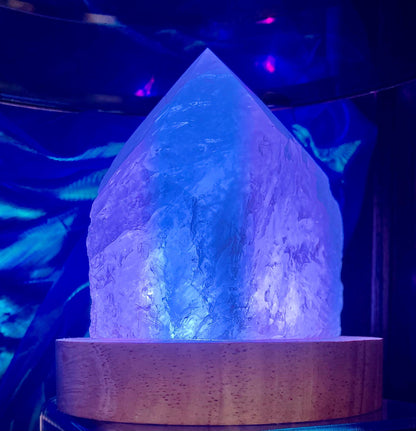 Pointe de cristal de roche semi-brut éclairée en violet sur un socle en bois