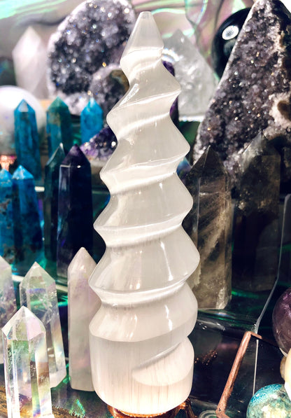 Spirale blanche de sélénite présentée devant des pierres brutes et des pointes de cristal
