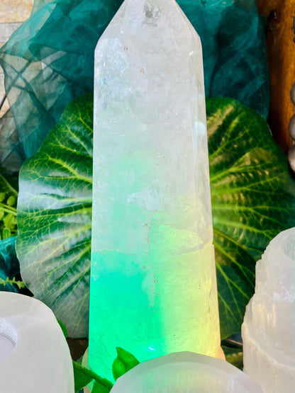 Grande pointe de quartz éclairée en vert à sa base, dans le décor de la boutique