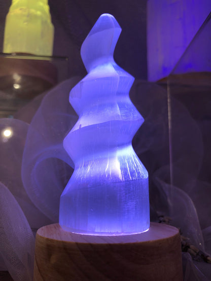 Lampe en spirale de sélénite éclairée en violet sur un socle en bois