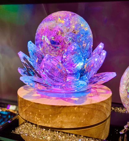 Sphère irisée posée dans un lotus à facettes, éclairée en rose et bleu sur un socle en bois
